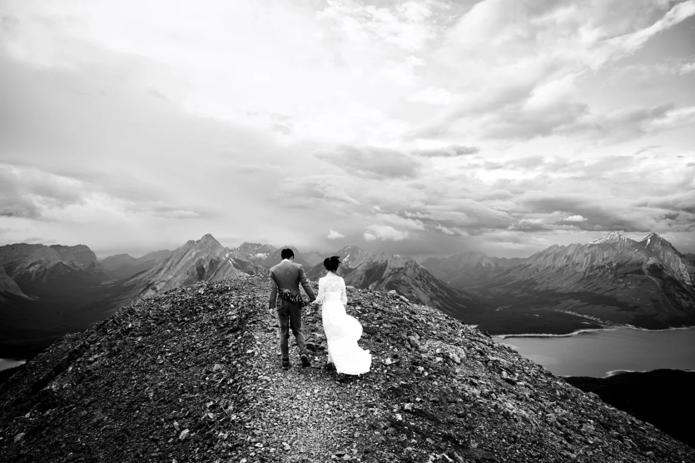 Photograph in black and white in the mountains on the bride and groom from behind.