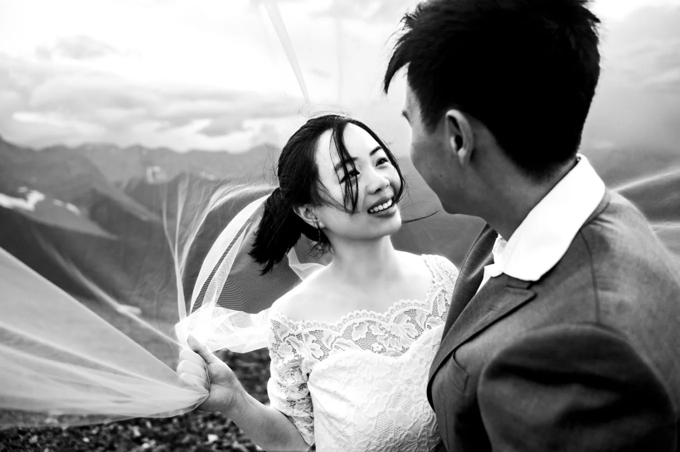 Black and white photograph under the veil of the bride and groom looking at each other.