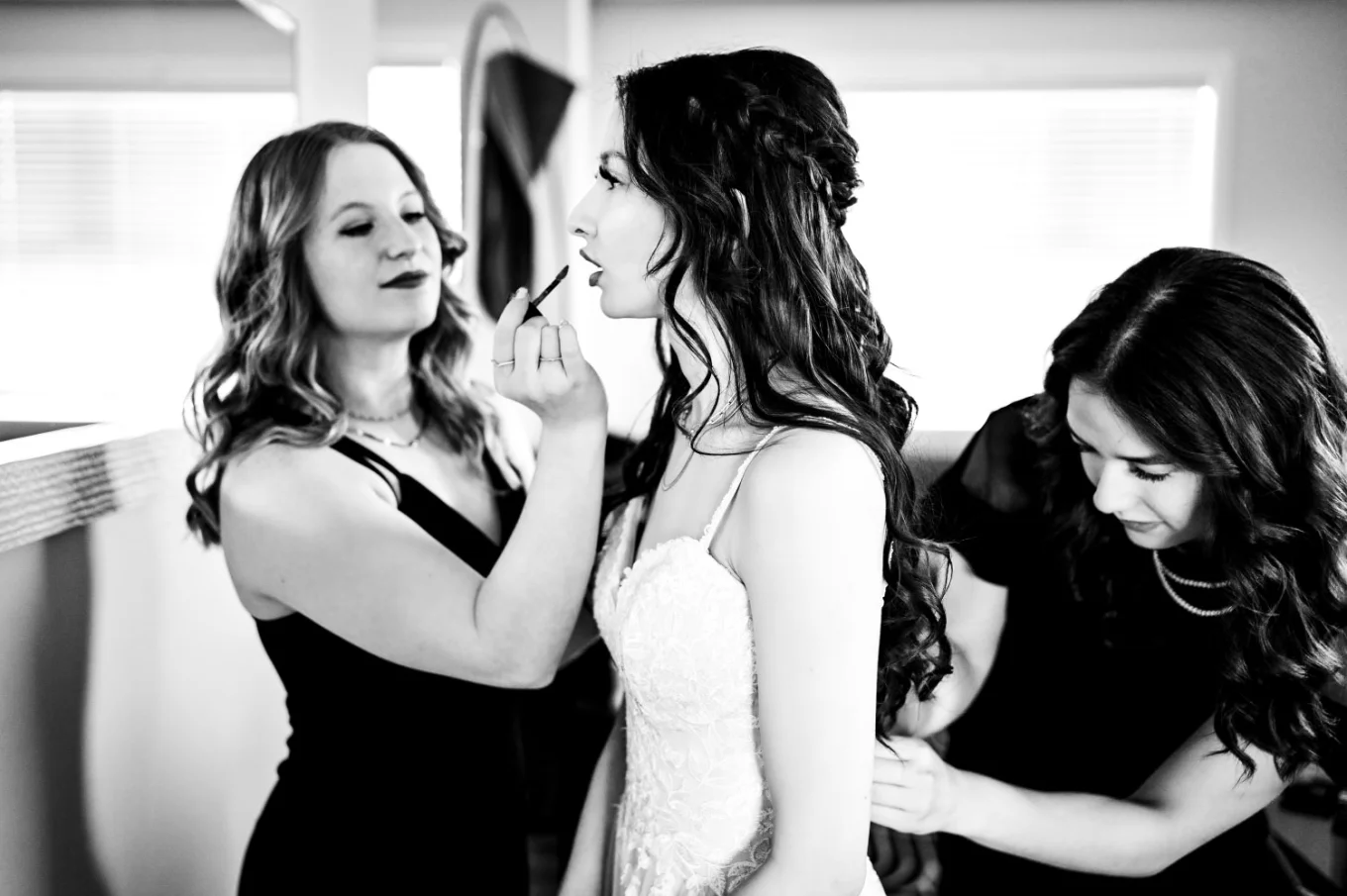 Bridesmaid help the bride to fix her make up and zip up the wedding dress