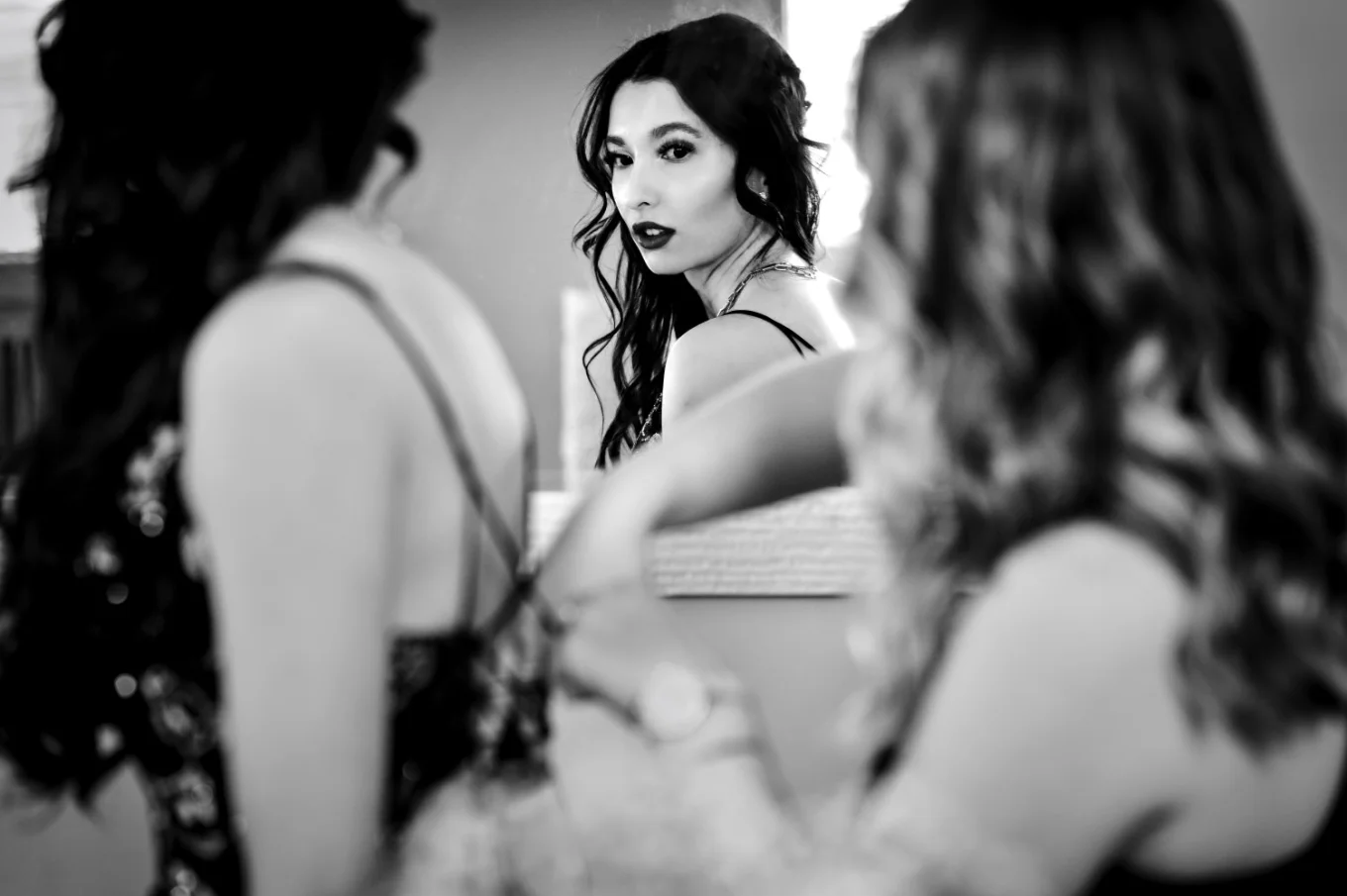 mirror reflection of the bride looking in the mirror while maid of honour fixes her wedding dress