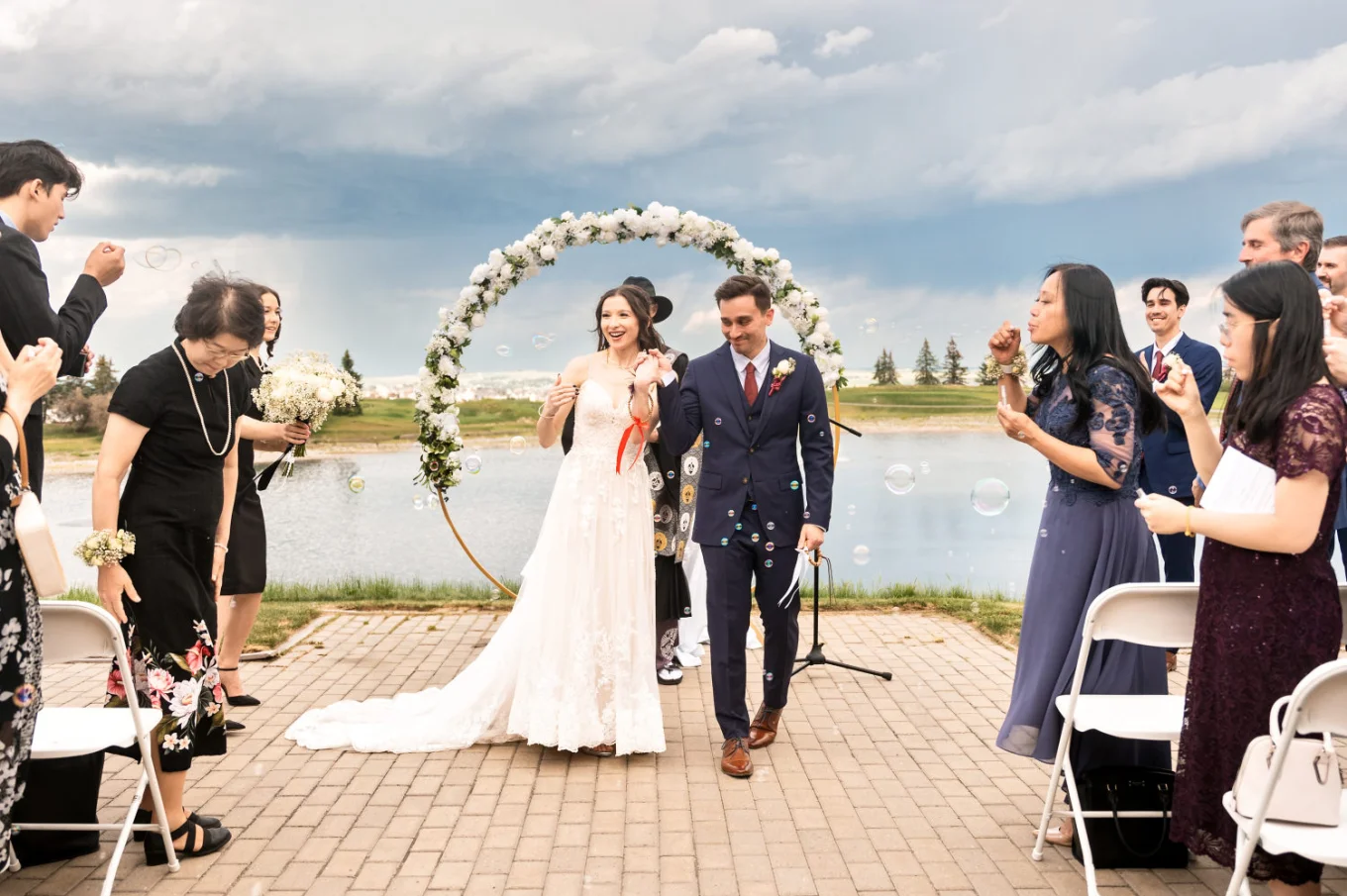 Bride and groom walking down the aisle in Calgary while wedding guests blow soap bubbles.