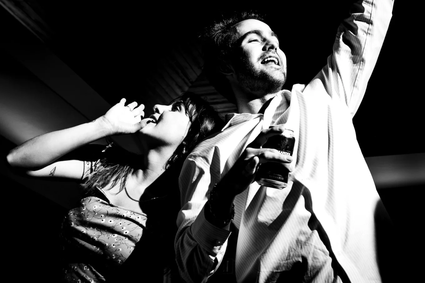 Man with the drink in his hand and a woman making fun of him, pretending that she drinks as well.
