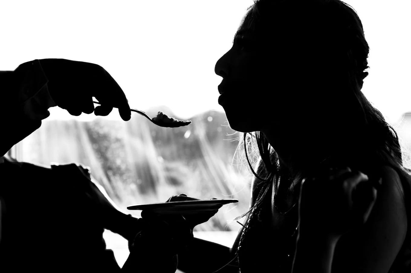 silhouette photograph of the bride being feed with the piece of the wedding cake