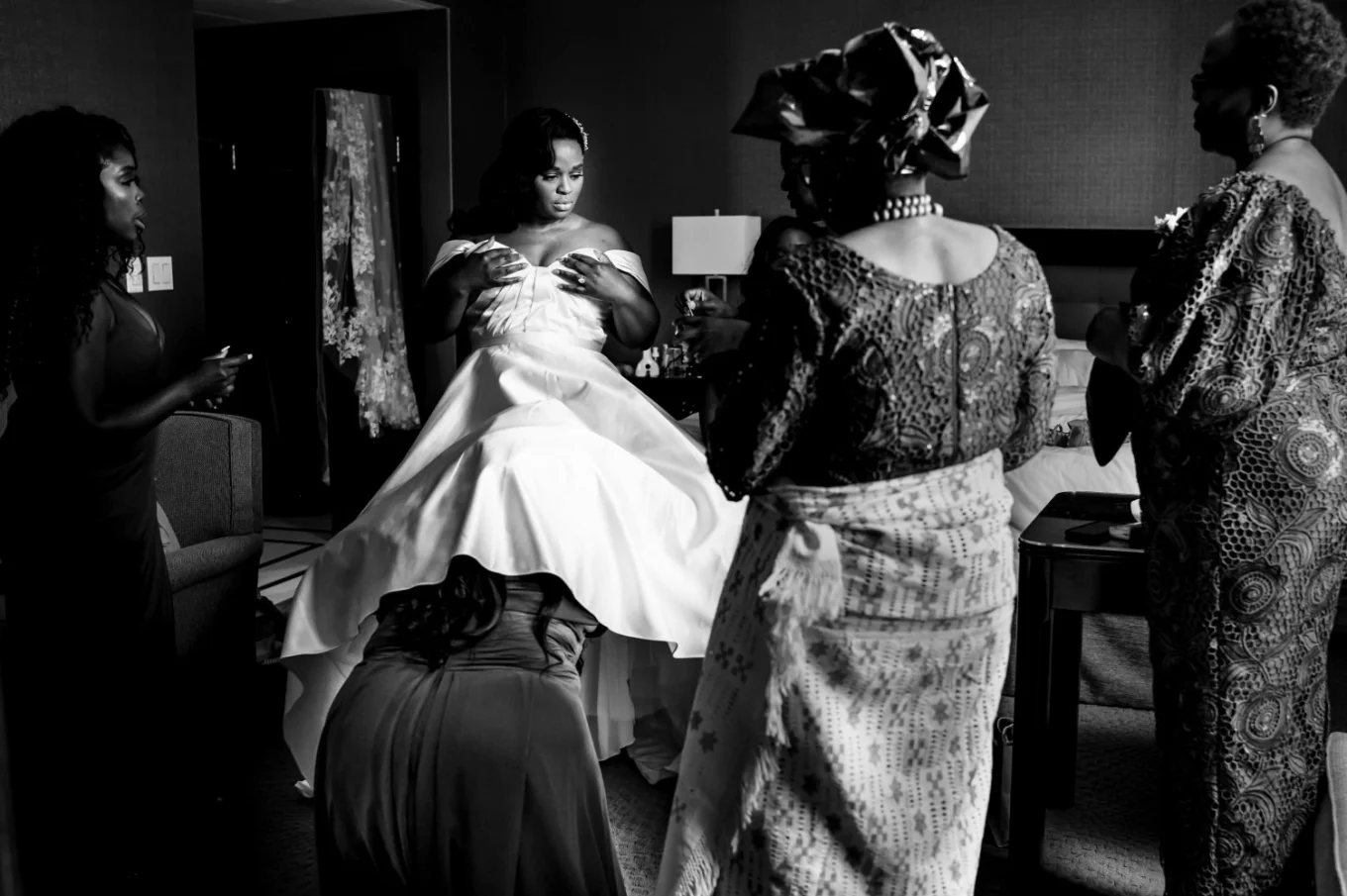 Maid of honour under the bride's wedding dress. Mother of the bride look at them.