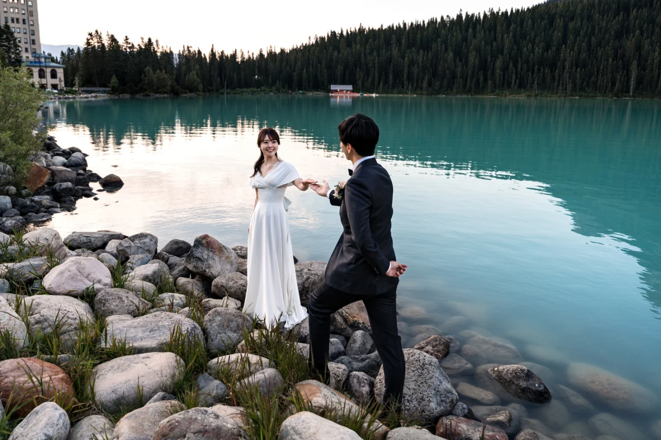 Groom helps his wife while walking on the rocks at the Lake Louise.