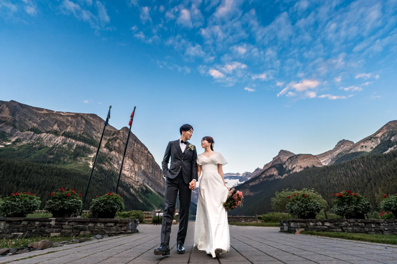 bride and groom walk on the pavement at the Lake Louise hotel. Above them blue sky.
