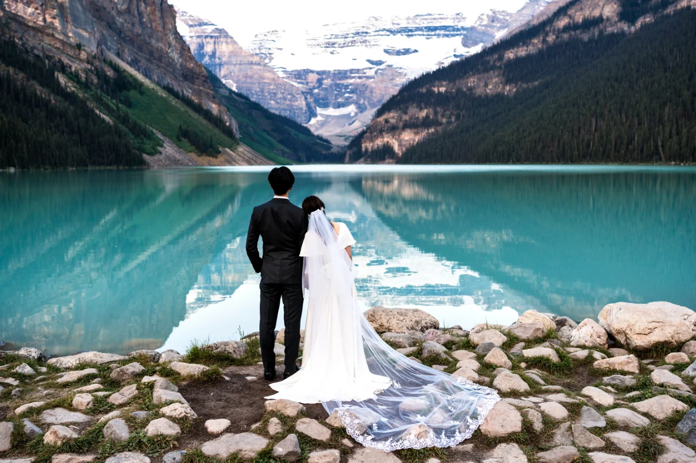 Newlyweds adore the beauty of the stunning Lake Louise. Photo taken from being by Banff Wedding Photographer.