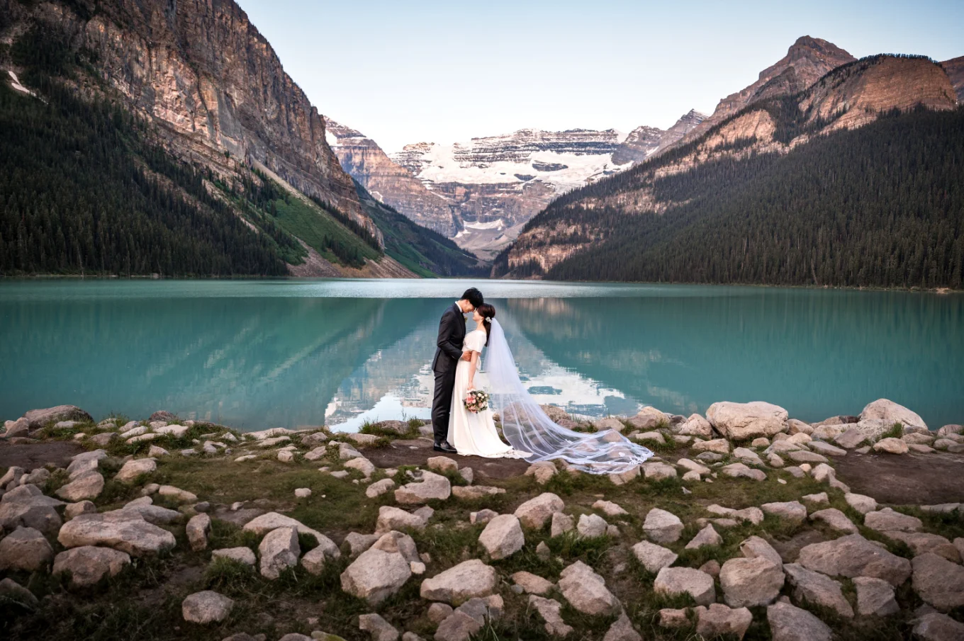 Newlyweds in a hug surrounded by the Canadian Rockies and turquoise Lake Louise.