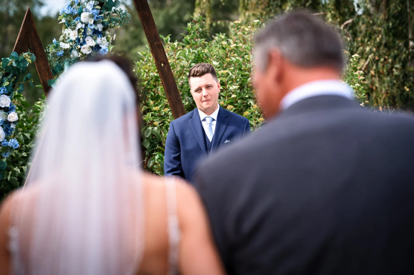 father of the bride walking her down the aisle while the groom look at her with love and excitment.