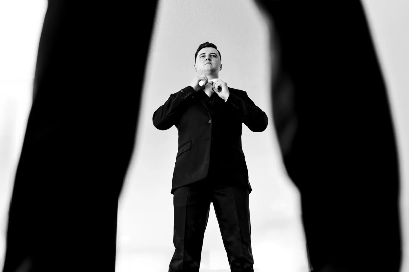 the groom fixes his tie. Photograph taken by Calgary wedding photographer through his legs