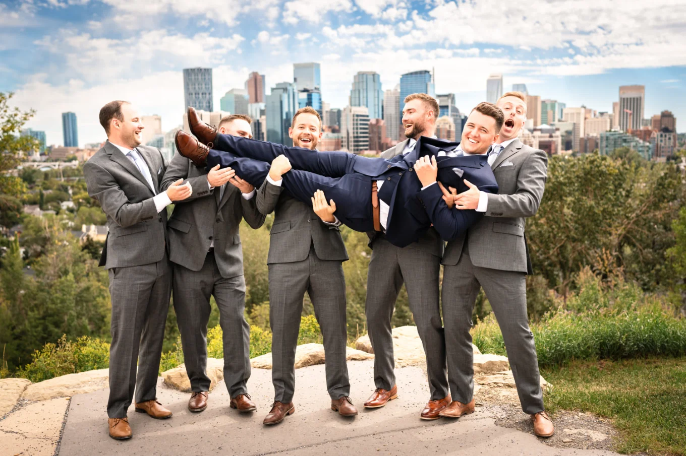 groomsmen take the groom on their hands. Photo taken against the city of Calgary.