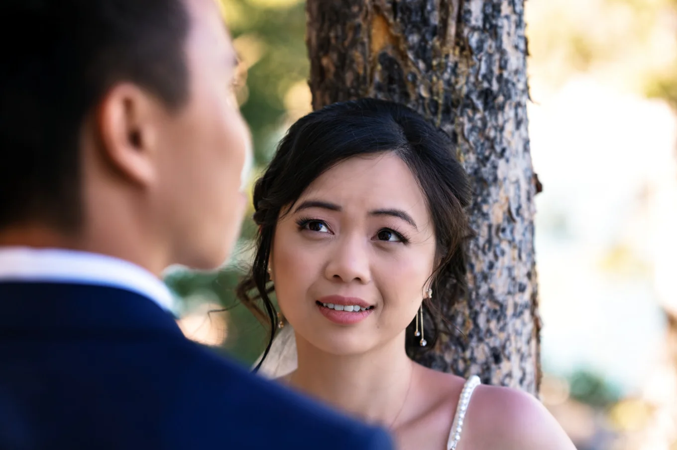 The bride lean over the tree and look at her husband at Minnewanka Lake in Banff.