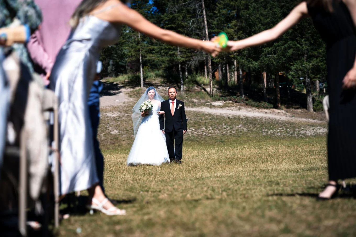 Father on the bride walks her on the aisle at Turner Mountain in Banff. Quest is passing the bubbles on hand to hand while they are walking.
