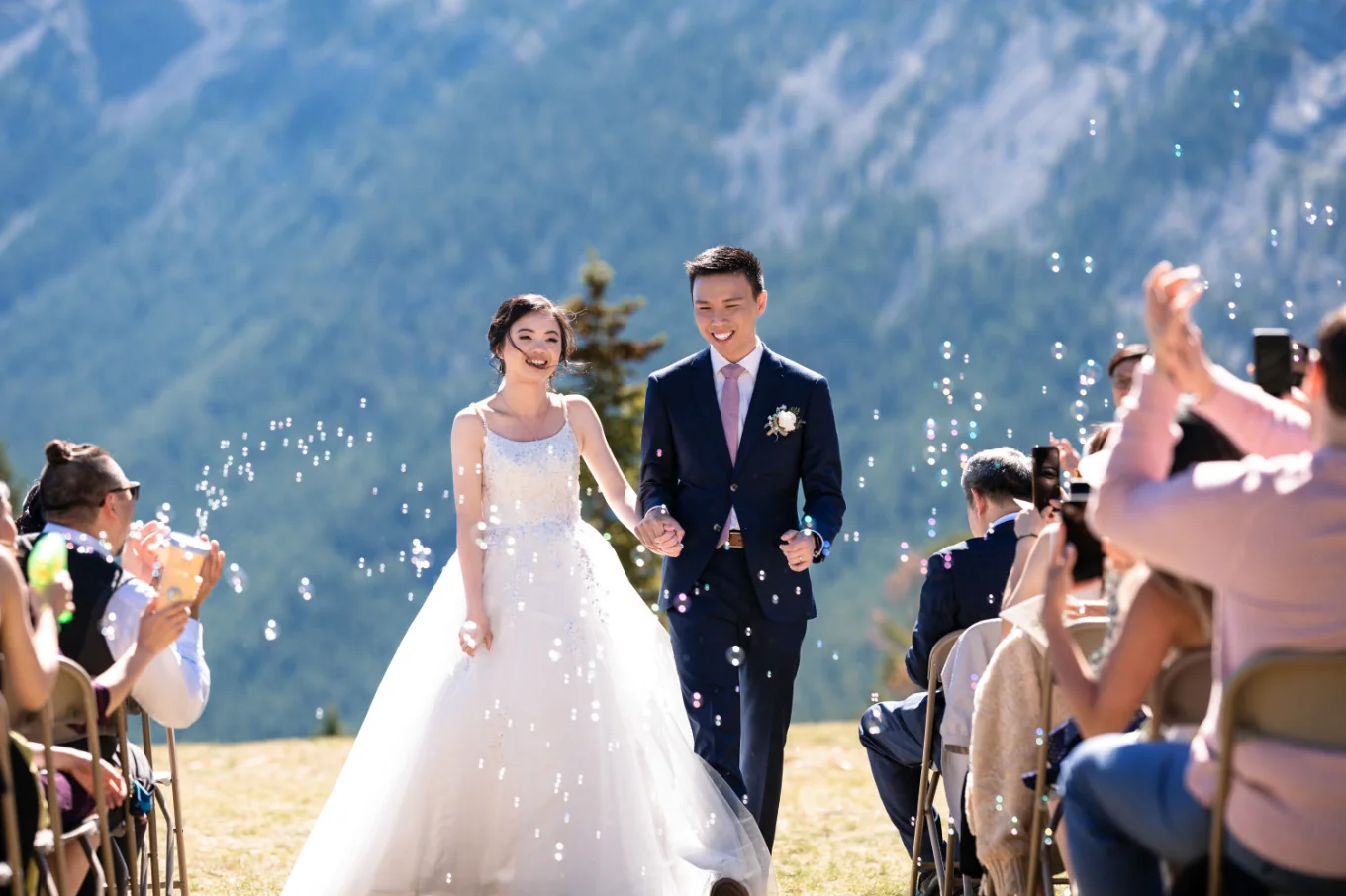 newlyweds walk out of the aisle holding their hands in Banff. All around them bubbles.