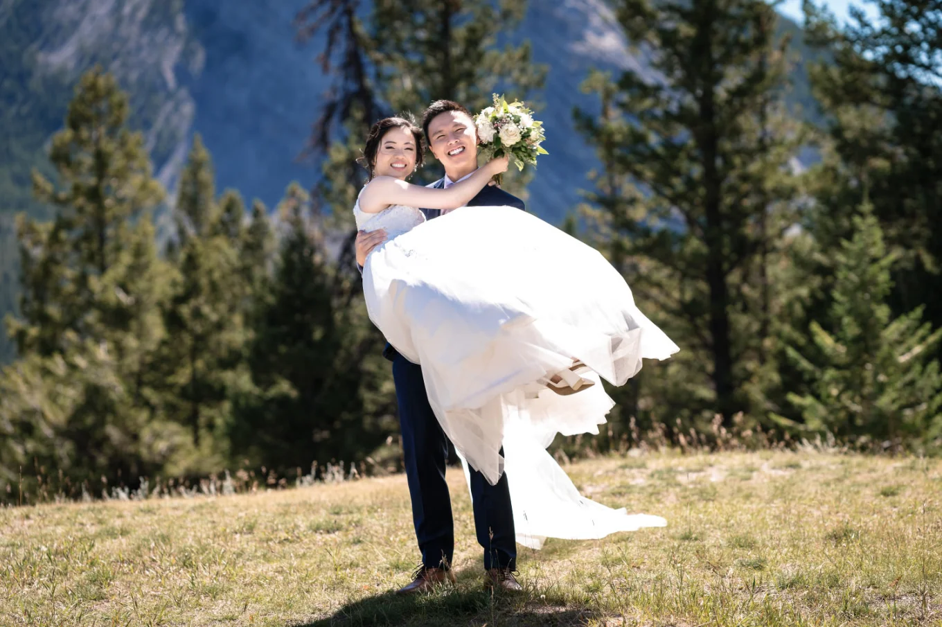 the groom carry his wife on the hands. They both smile. Moment captured by banff wedding photographer.