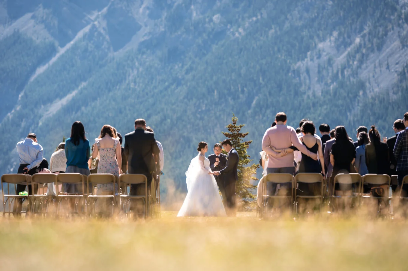 Banff Wedding Photography at Tunnel Mountain. Photograph at the wedding ceremony of the banff officiant , newlyweds and the quests standing and watching then.