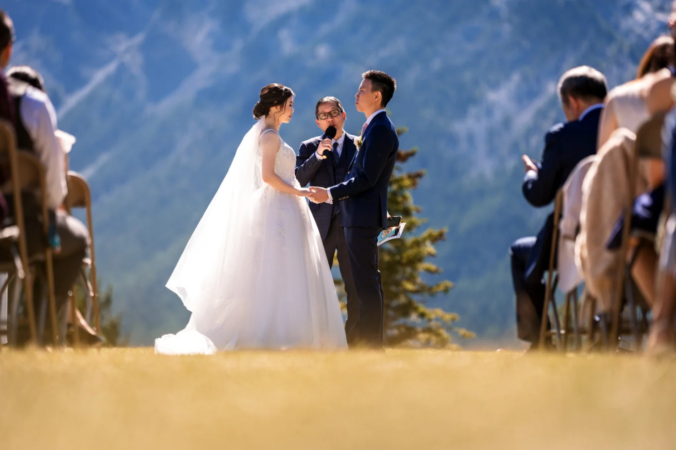 newlyweds holding hands and the officiant holding the micophone on the Tunnel Mountain in Banff.