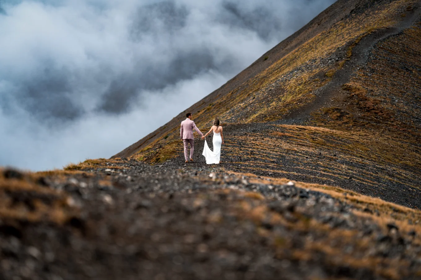 Bride and groom hold their hands and walk at the mountain ridge in the Canadian Rockies.