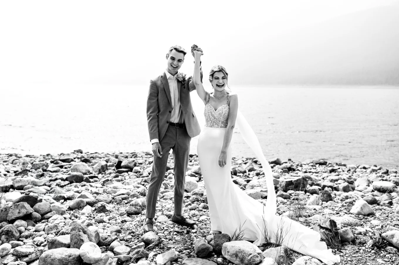 A picturesque scene of a bride and groom standing on rocks by the water, radiating love and happiness.