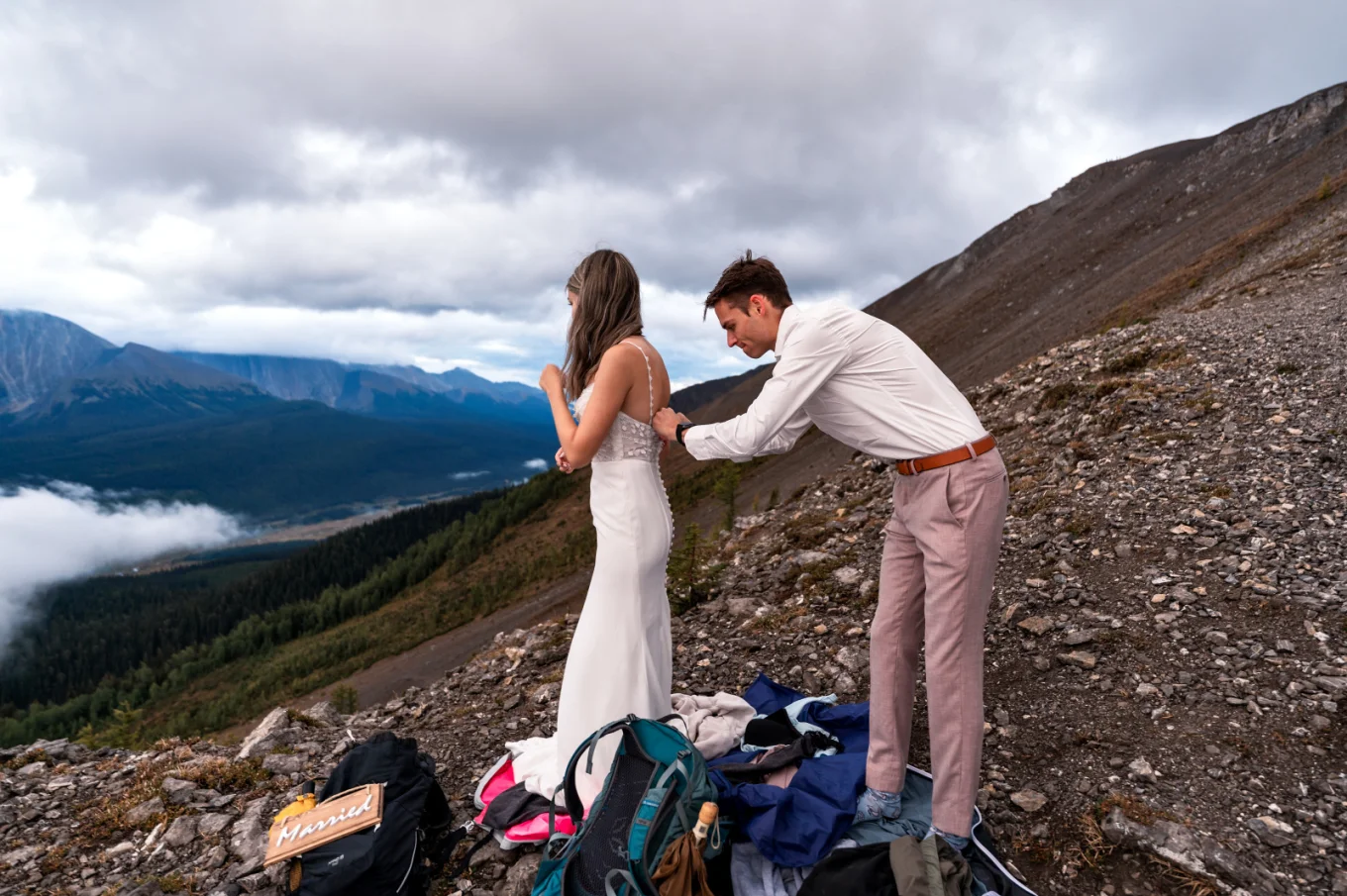 Groom helps the bride to zip her wedding dress before the wedding session in the mountains.