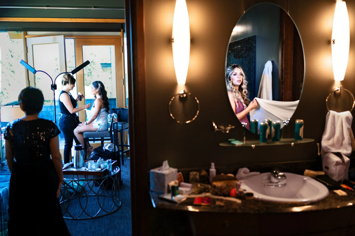 Bride getting her make up done and the bride's maid look at the mirror on the wedding day in Calgary
