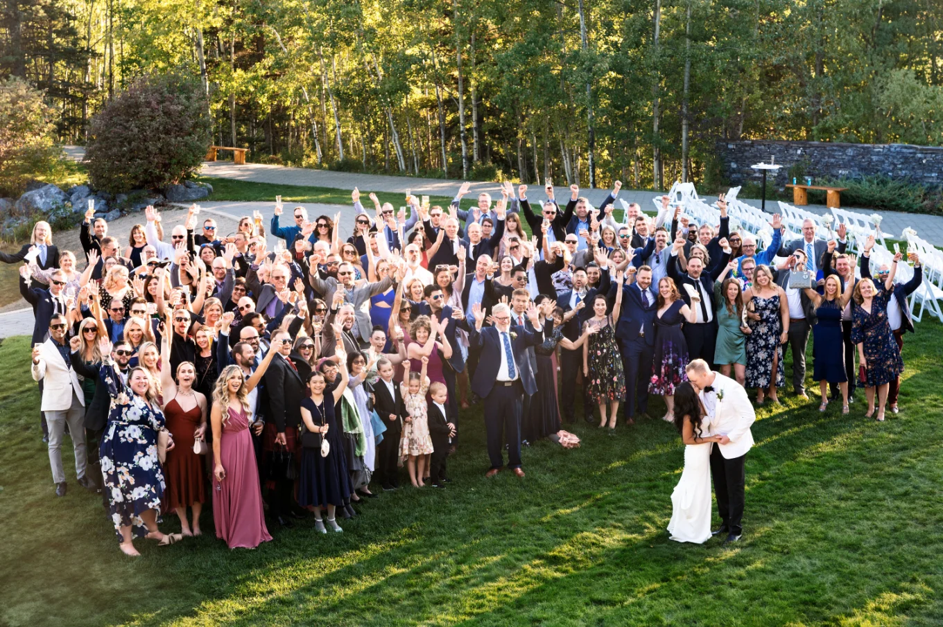 Wedding group photo with all the wedding guests while bride and groom share a kiss