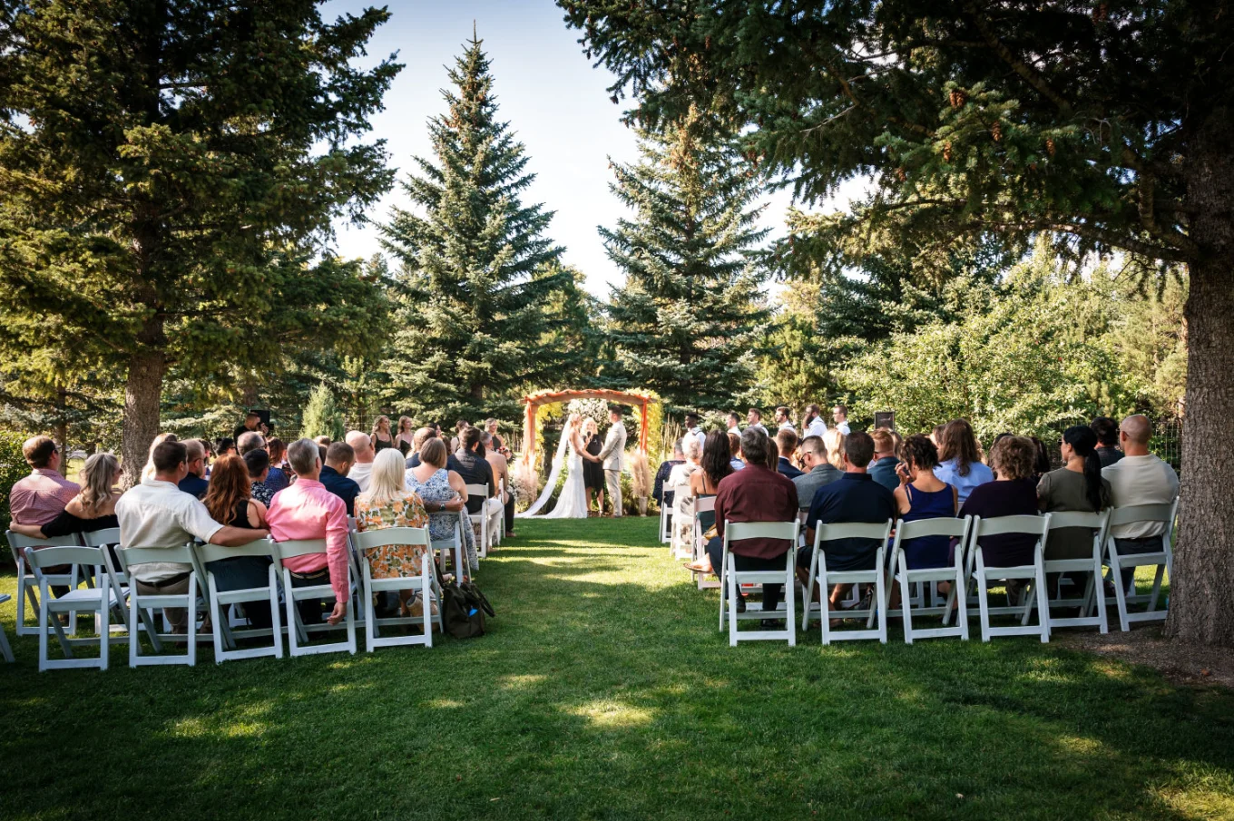 Wedding ceremony in Waterton. Quests sit on the white chairs while bride and groom echance their vowes.