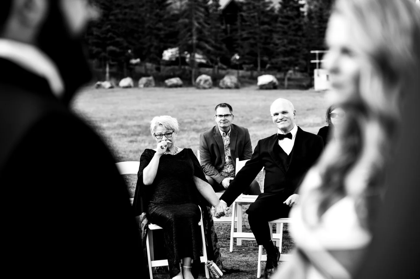 Parents of the bride hold their hands and look at their kids getting married in Banff