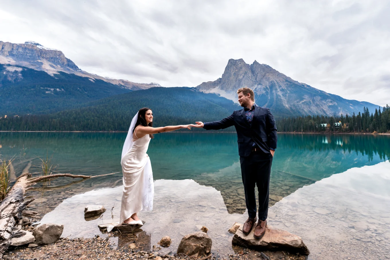 Groom helps the bride to walk on the rocks by Emerald Lake.