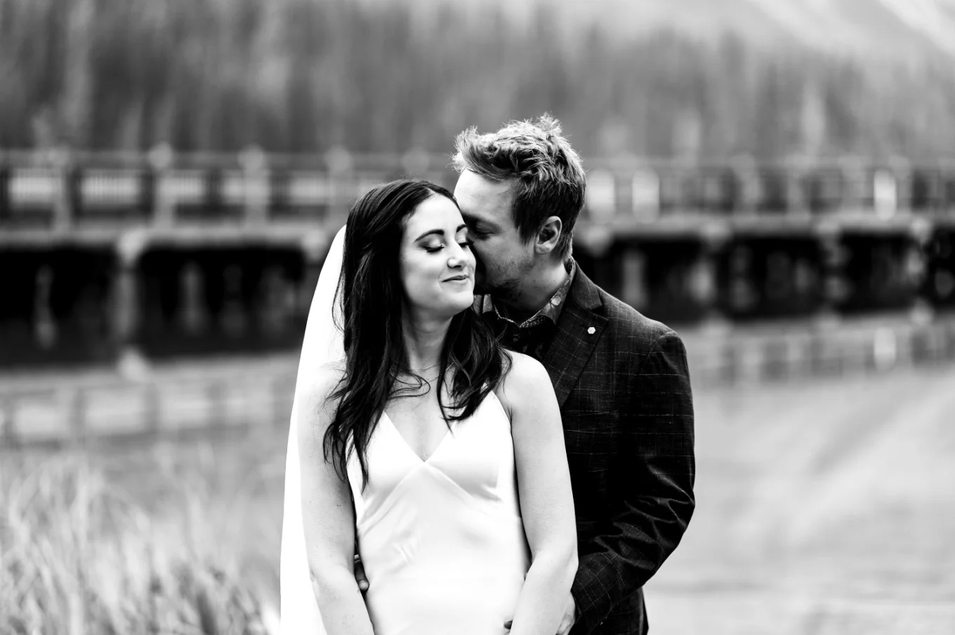 Groom hugs the bride from behind and kisses her.