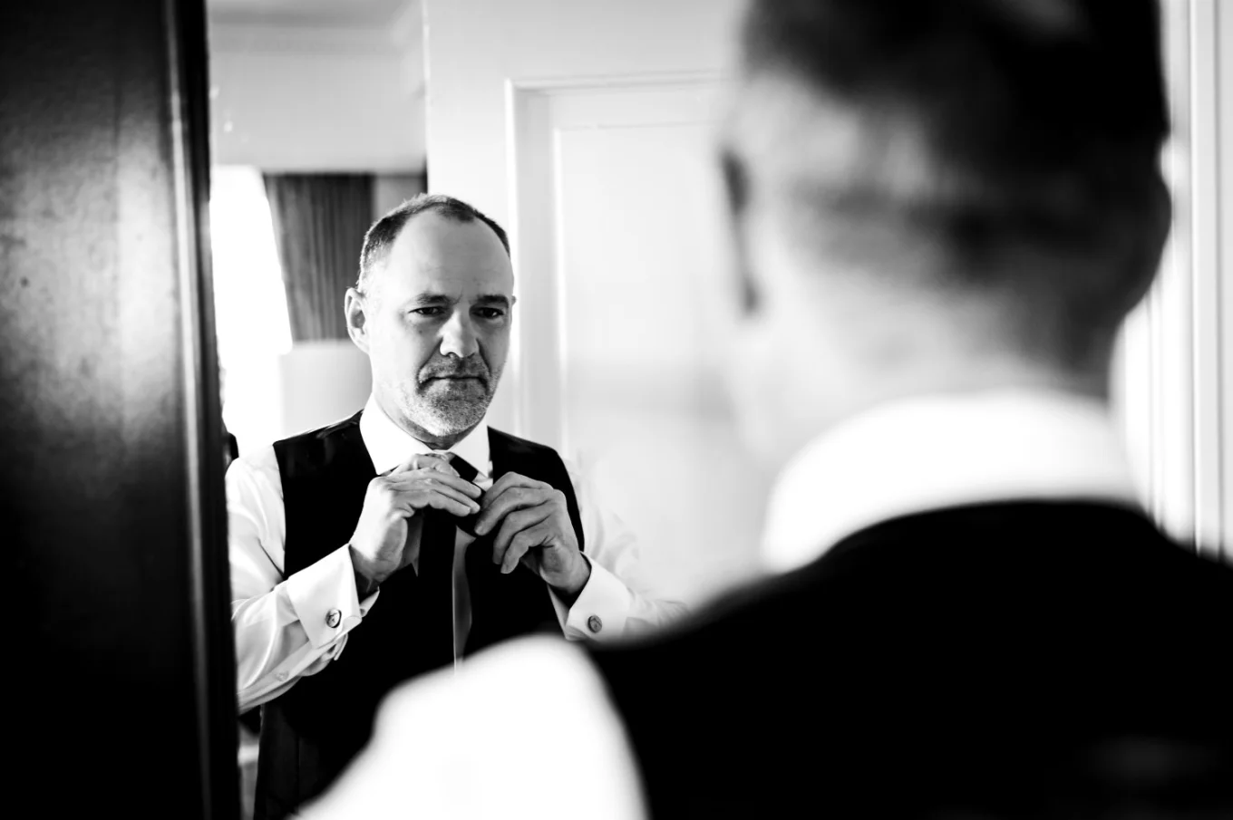Groom fixes his tie in front of the mirror.