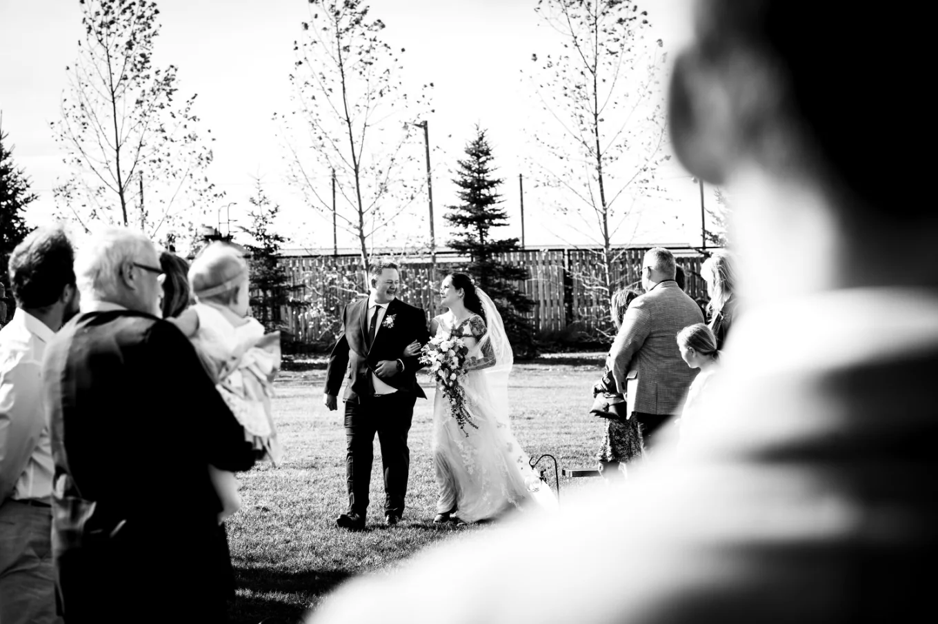 Father walks the bride down the aisle in Calgary while the groom and quests looking at them .