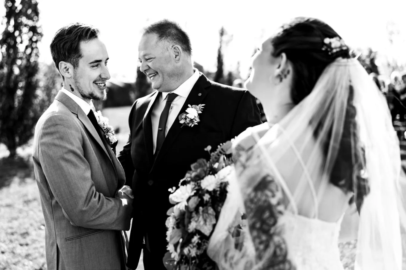The father of the bride giver her away to the groom. They both laugh while talking.