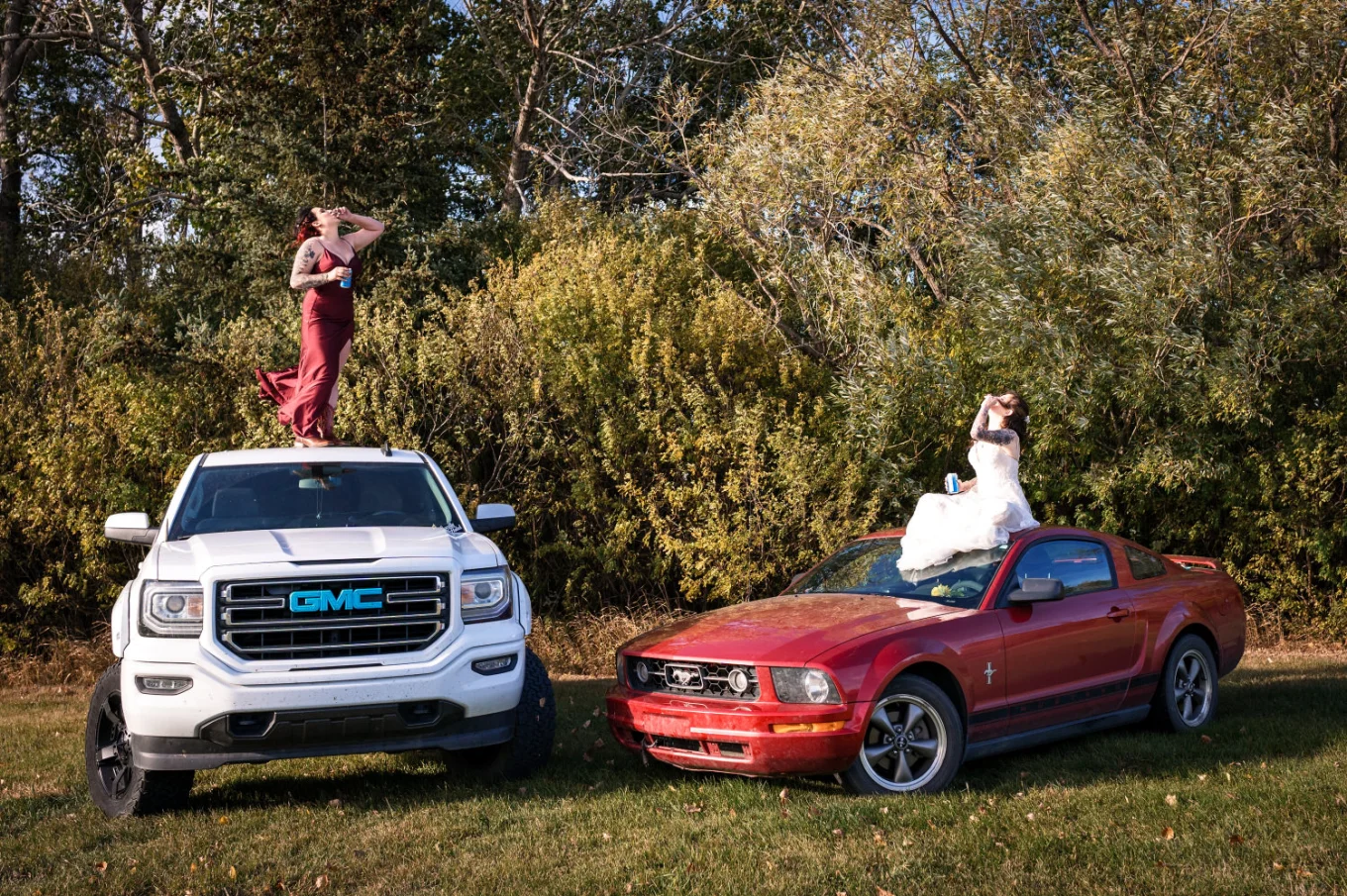 Bride and bridesmaid sitting on their cars and drink a beer.