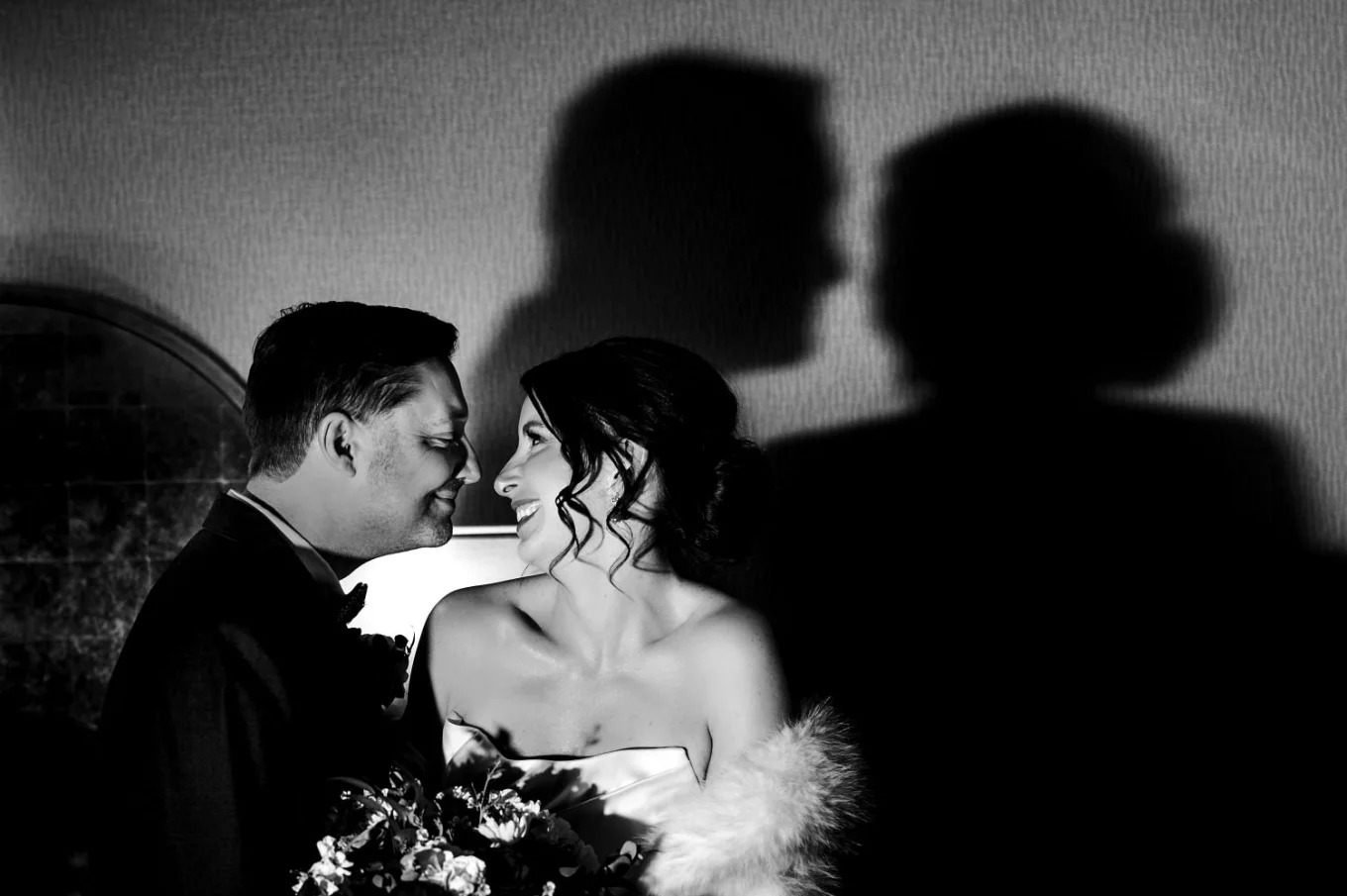 Bride and groom look at each other with their shadow on tthe wall