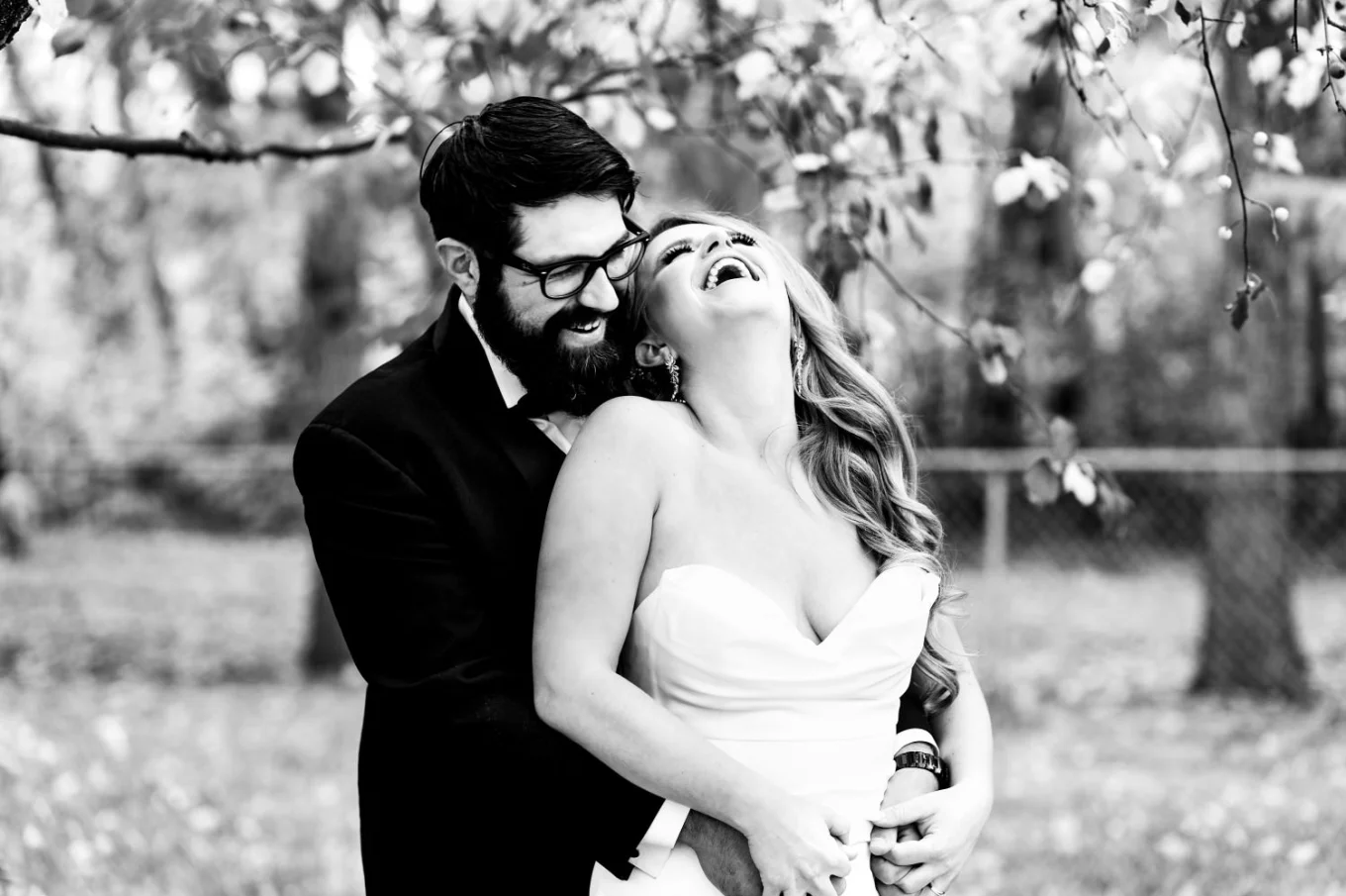 The groom hugs his wife from behind. She laughs in the park in Edmonton.
