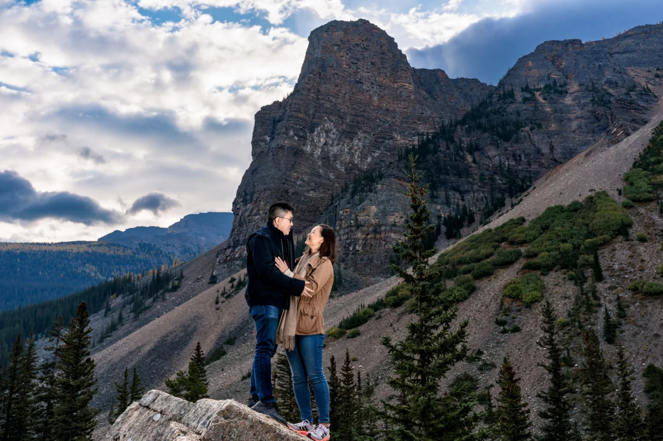 engaged couple in a hug standing at a huge rock in the mountains in Canada