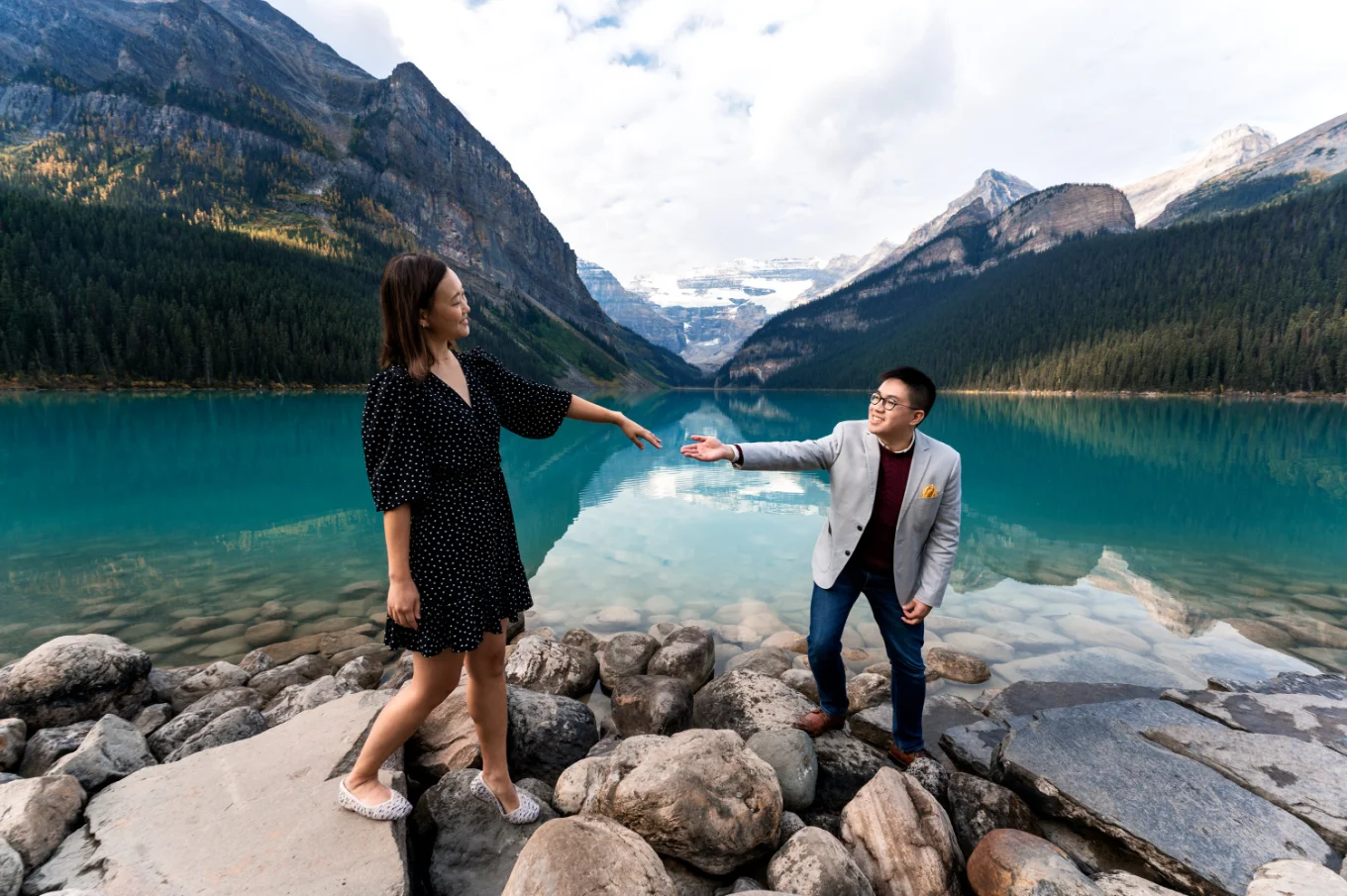Man helps his fiancee to walk on the rocks at beautiful Lake Louise.