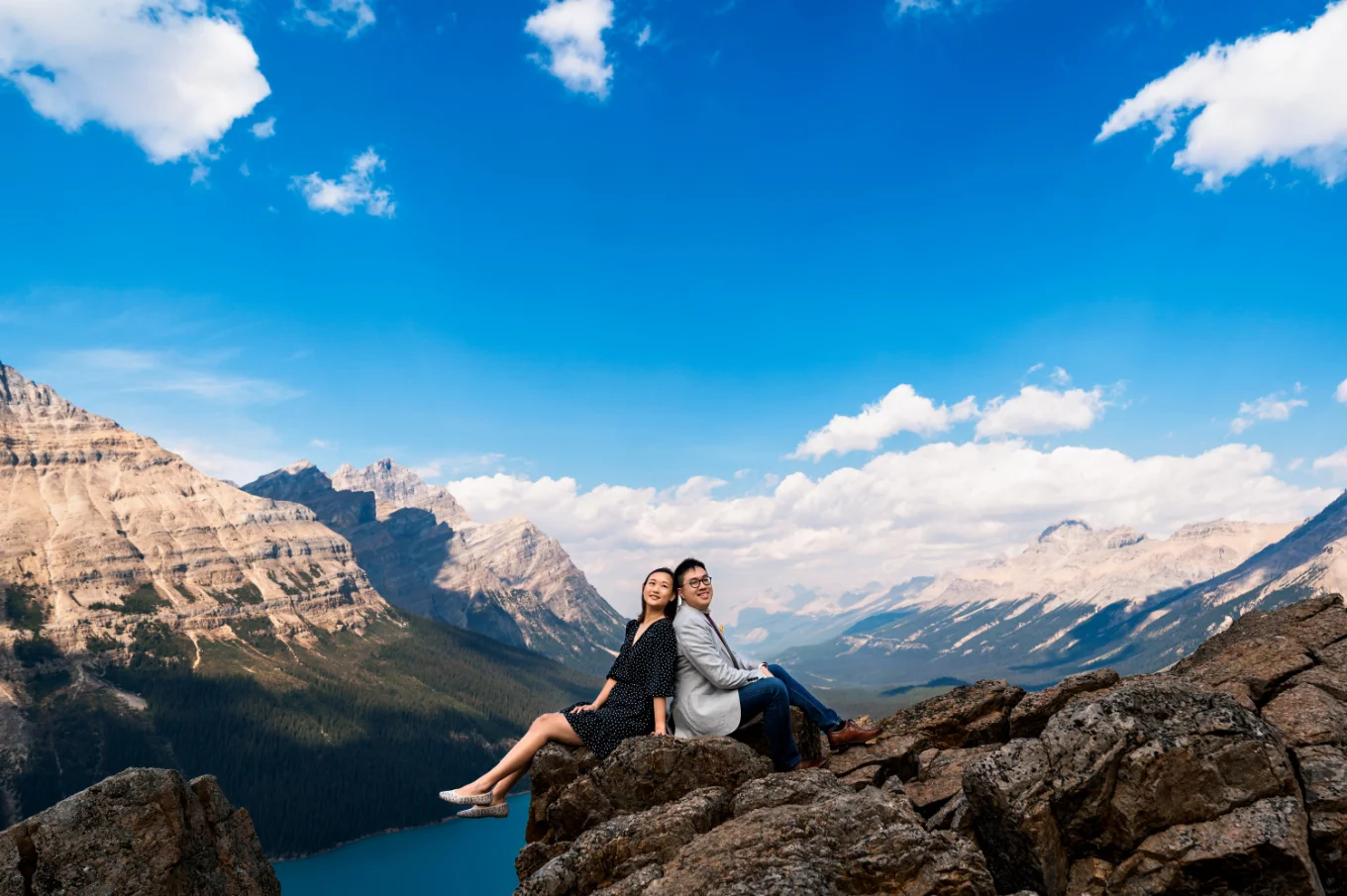 Engaged couple sitting back to back in the mountains at Peyto Lake