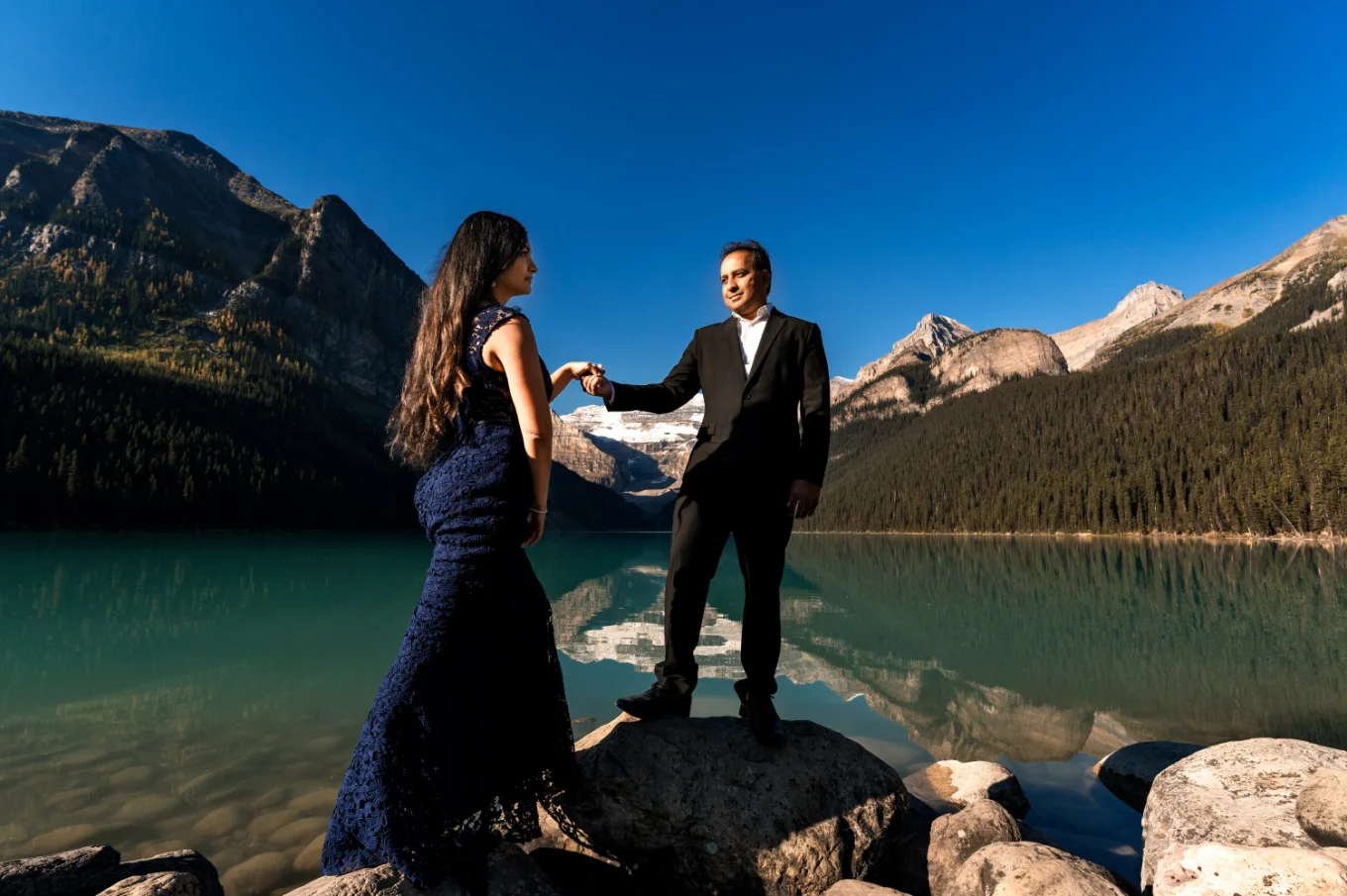 Husband leads her walking wife at the shore of Lake Louise.