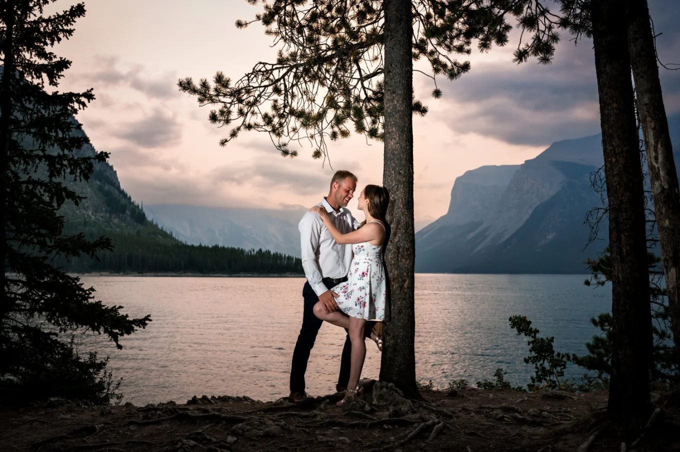 Romantic Banff Engagement photography of the woman leaning over the tree and her fiancee hugging her