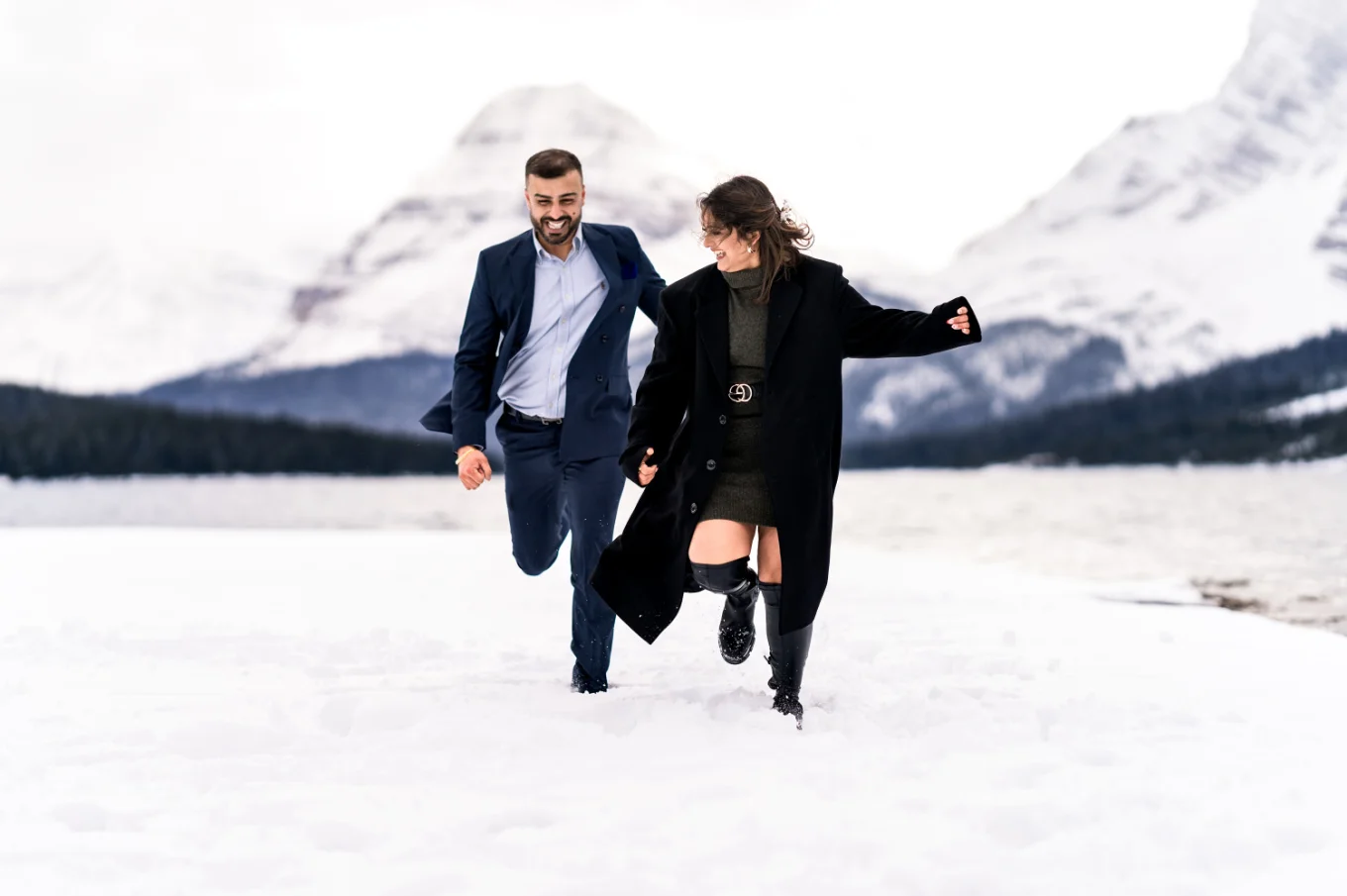 Engaged couple run and have lots of fun in the snow in Banff National Park.