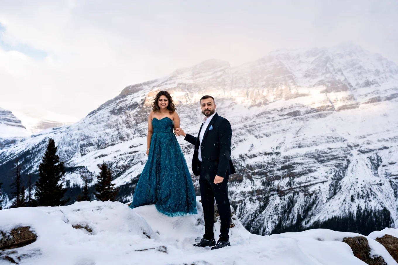 Gentleman helps his fiancee to walk down the small hill covered with snow in Banff National Park