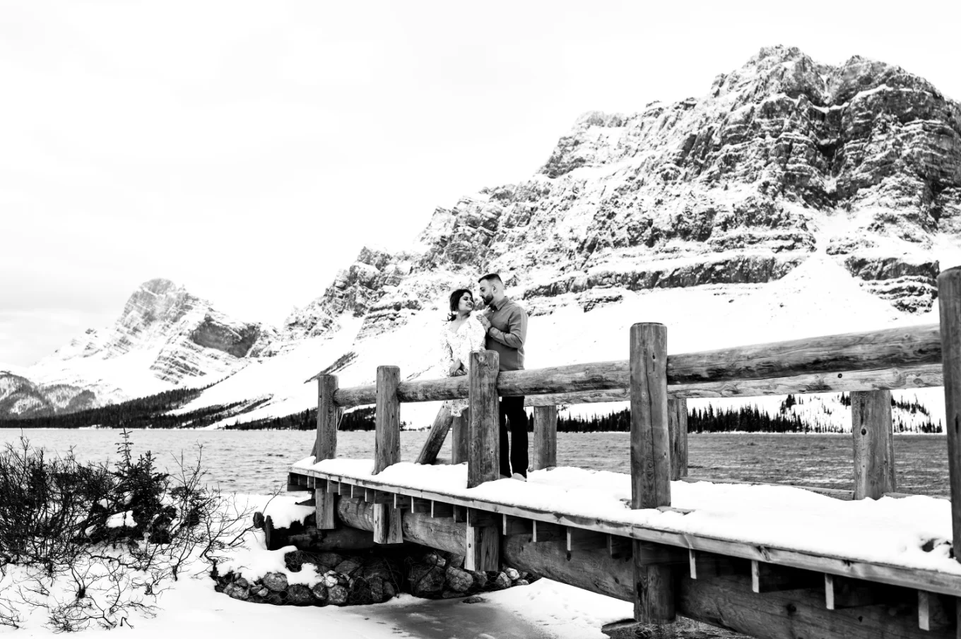 two lovers stand at the wooden bridge at Bow Lake against huge mountain covered with snow.