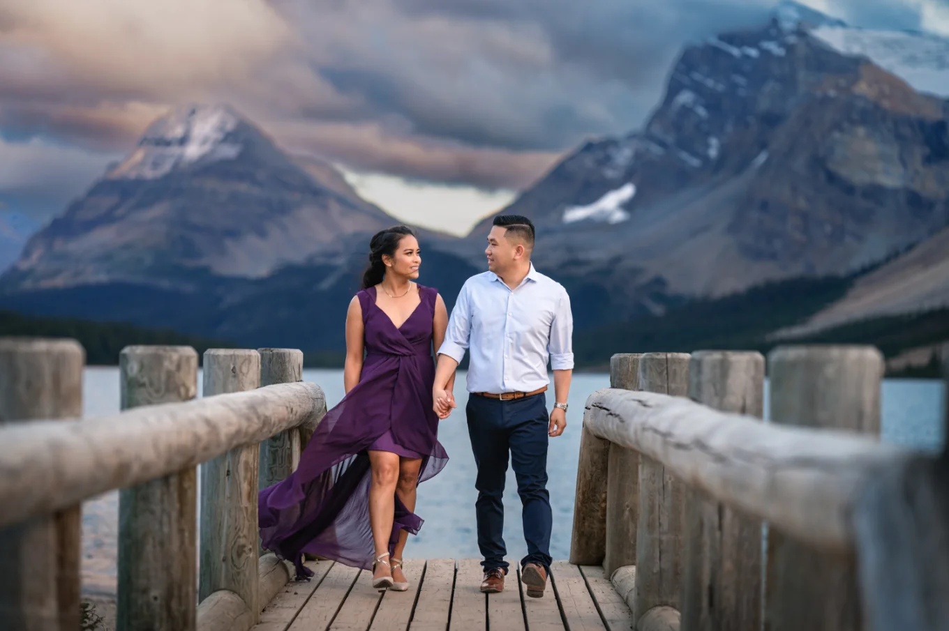 Man and lady in a purple dress walking on the wooden bridge in Banff.