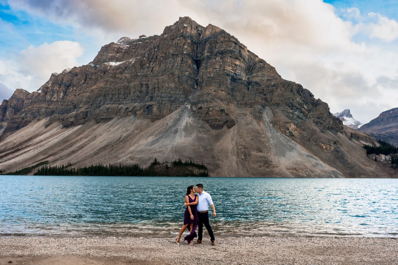 Engaged couple dances at the shore of Bow Lake against huge mountain.