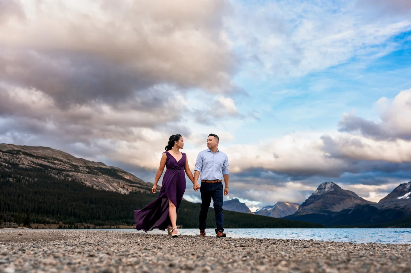 Engaged couple walks at the shore of Bow Lake during coloreful sunset.