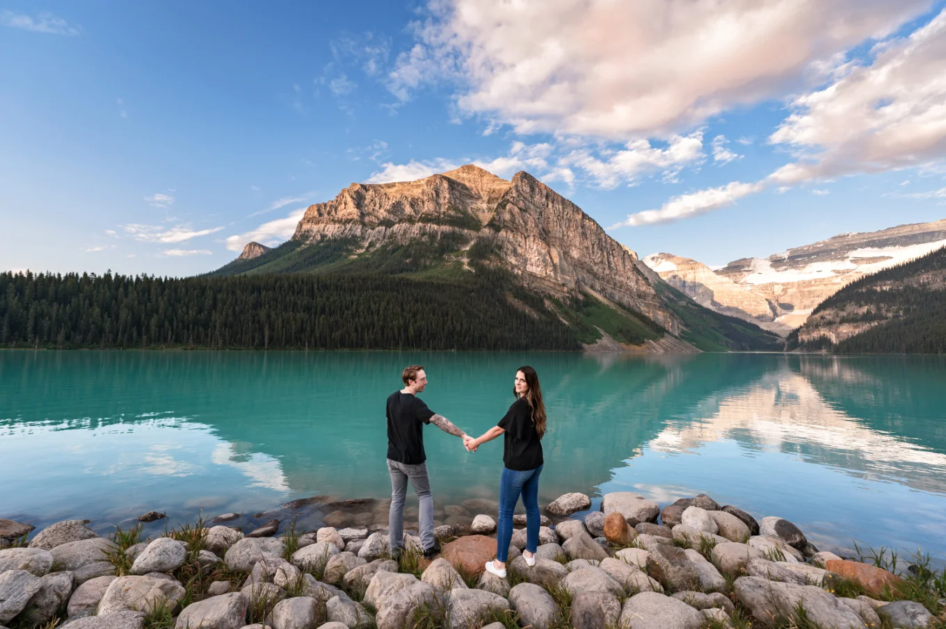 Engaged couple hold hands and adore the stunning view of the Rocky Mountains at Lake Loyuse.