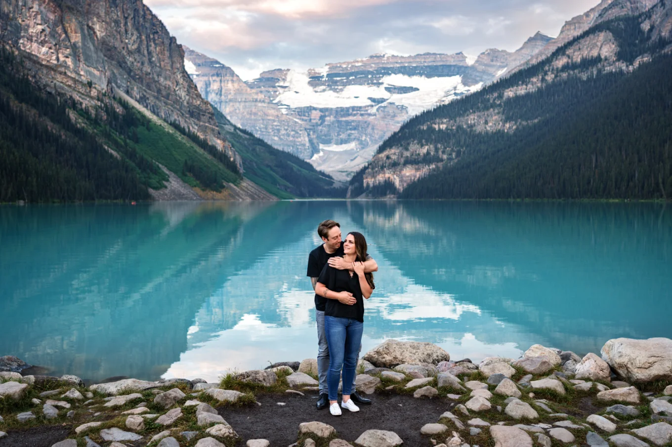 Lake Louise Engagement Photography of the couple in a hug at the shore of turquoise lake.