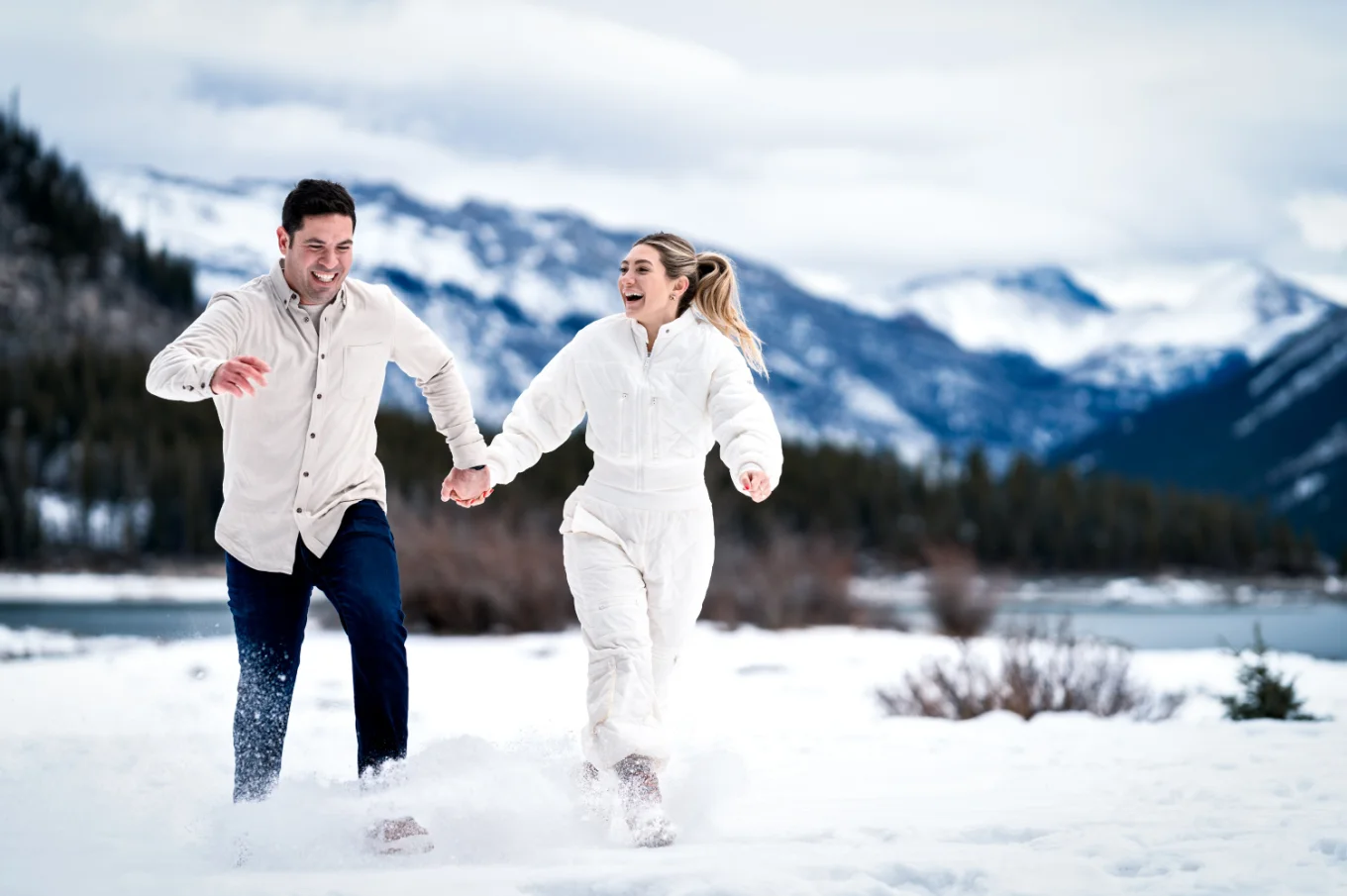Fun time of the engaged couple runnn i the snow at Minnewanka Lake